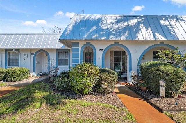 view of front facade with a front lawn, metal roof, and stucco siding