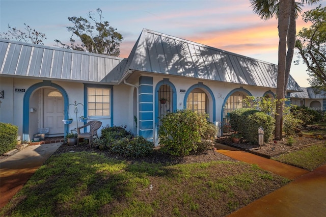 view of front of house featuring metal roof, a lawn, and stucco siding