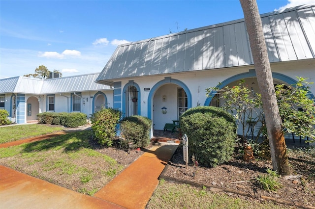 view of front facade featuring a standing seam roof, a front lawn, metal roof, and stucco siding