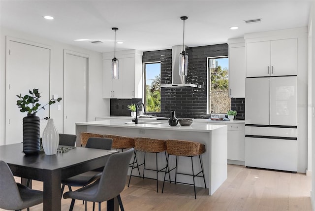 kitchen featuring an island with sink, decorative light fixtures, light countertops, white fridge, and white cabinetry