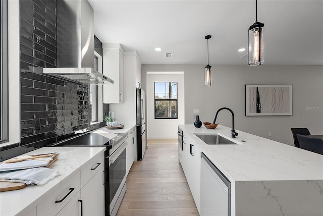 kitchen with a sink, electric stove, wall chimney exhaust hood, an island with sink, and decorative light fixtures