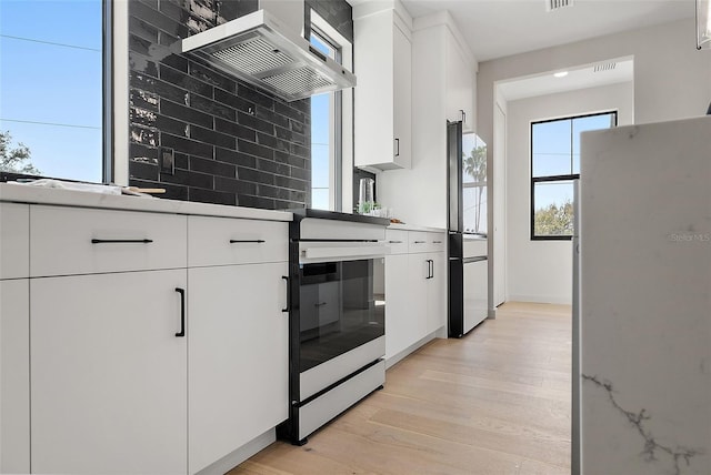 kitchen with exhaust hood, light wood-style floors, white cabinets, light countertops, and fridge