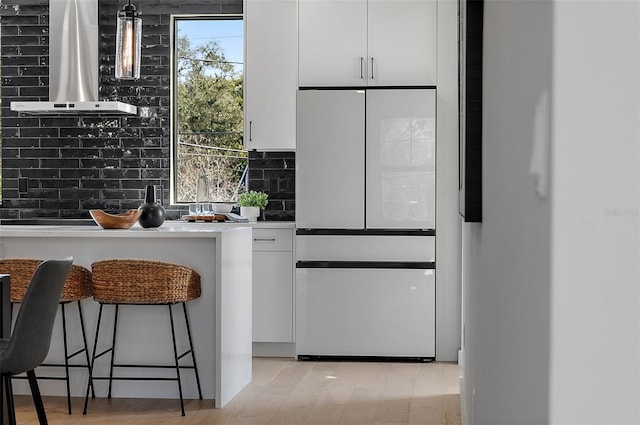 kitchen featuring white cabinets, light countertops, wall chimney range hood, decorative backsplash, and white fridge