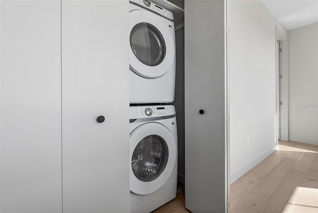 laundry room with laundry area, baseboards, light wood finished floors, and stacked washer / drying machine