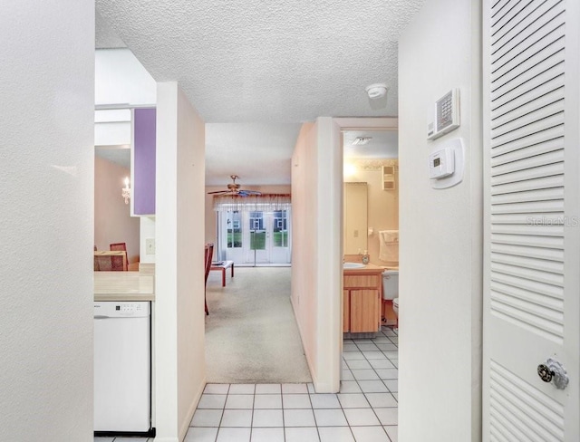 hall with light tile patterned floors, a textured ceiling, light carpet, and a sink