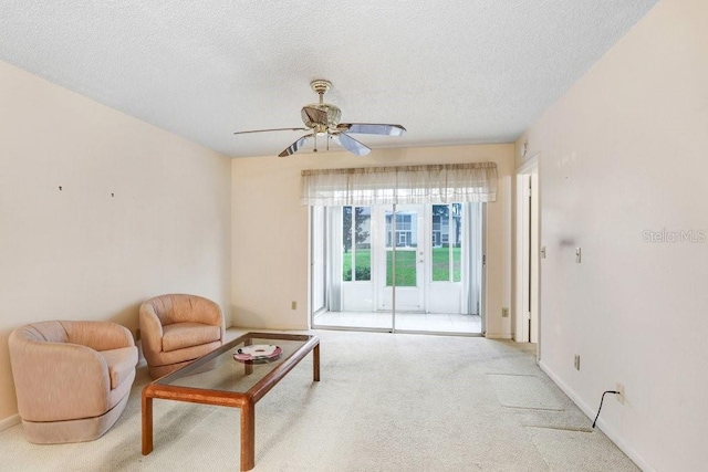 living room featuring baseboards, a ceiling fan, a textured ceiling, and light colored carpet