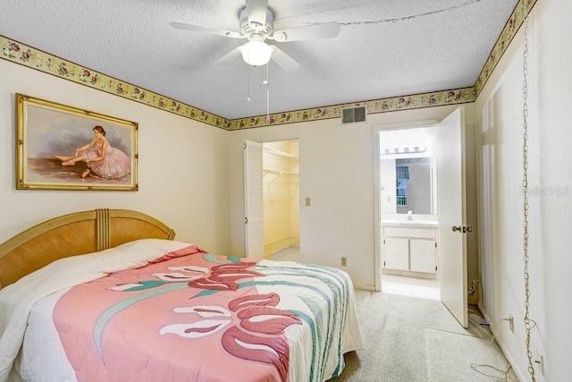 bedroom with ensuite bath, visible vents, a textured ceiling, and light colored carpet