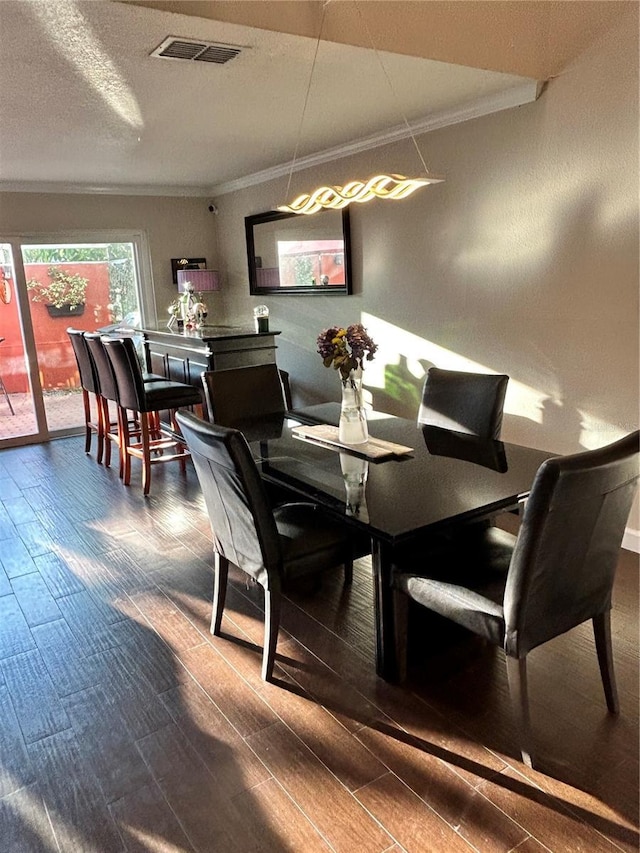 dining space featuring dark wood-style floors, visible vents, a textured ceiling, and ornamental molding