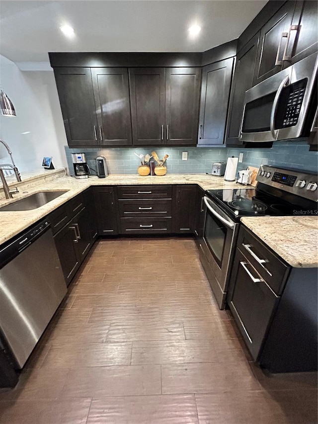 kitchen featuring a sink, backsplash, appliances with stainless steel finishes, and light stone countertops