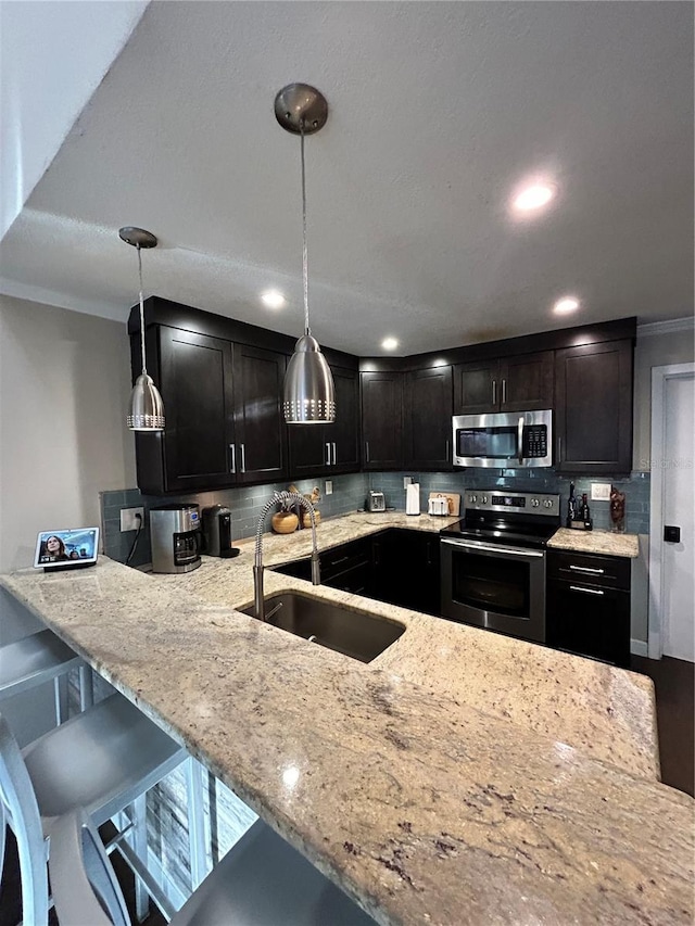 kitchen with backsplash, decorative light fixtures, light stone counters, appliances with stainless steel finishes, and a sink