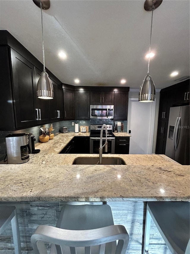 kitchen with pendant lighting, light stone counters, tasteful backsplash, and stainless steel appliances