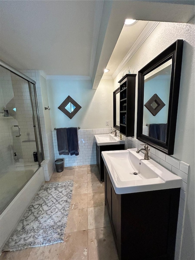 bathroom with enclosed tub / shower combo, two vanities, a sink, crown molding, and tile walls