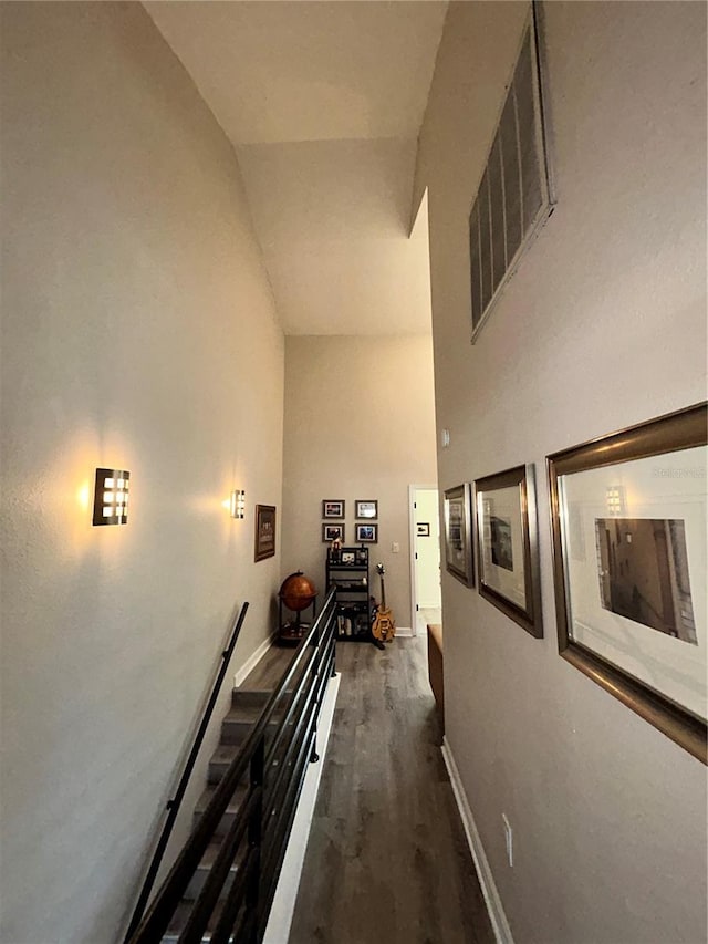 hallway featuring baseboards, visible vents, high vaulted ceiling, dark wood finished floors, and an upstairs landing