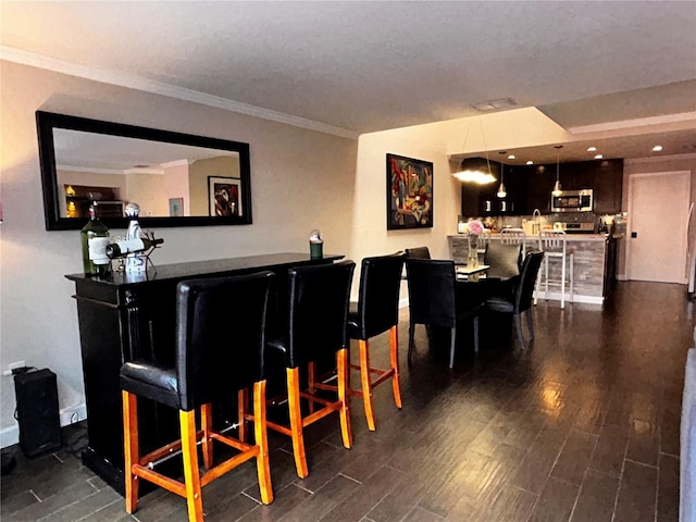 bar with dark wood-type flooring, pendant lighting, stainless steel microwave, a bar, and crown molding