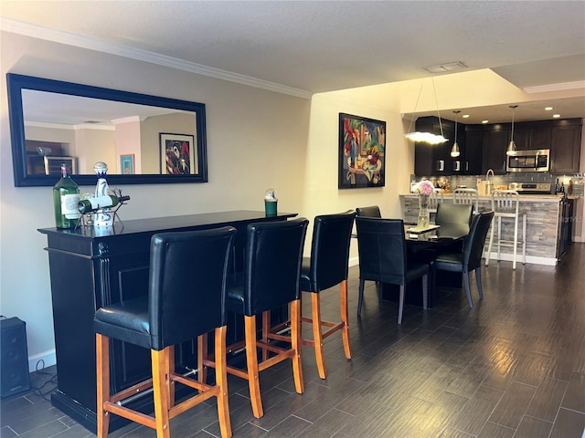 bar with dark wood-style flooring, crown molding, stainless steel microwave, a dry bar, and decorative light fixtures