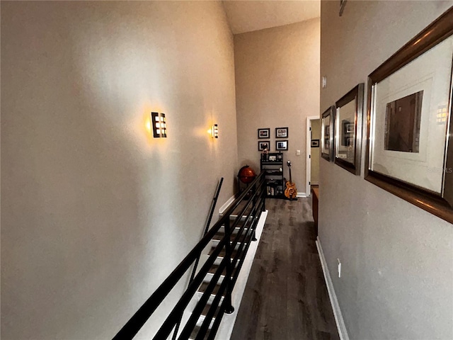 corridor with a high ceiling, an upstairs landing, dark wood-style floors, and baseboards