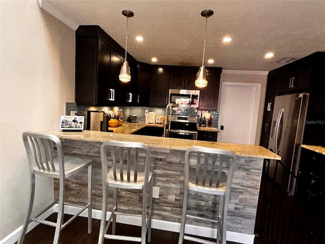 kitchen featuring light stone counters, appliances with stainless steel finishes, pendant lighting, and a peninsula