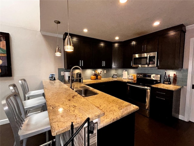 kitchen featuring light stone countertops, a peninsula, a sink, appliances with stainless steel finishes, and tasteful backsplash