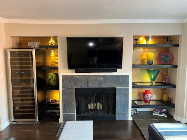 living area with beverage cooler, built in features, crown molding, baseboards, and a tile fireplace