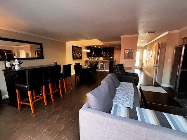 living room featuring baseboards, visible vents, dark wood-style flooring, a bar, and crown molding