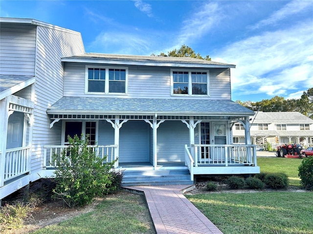 view of front of property with a shingled roof, a front yard, and covered porch