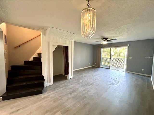 unfurnished living room featuring a textured ceiling, wood finished floors, a ceiling fan, baseboards, and stairway