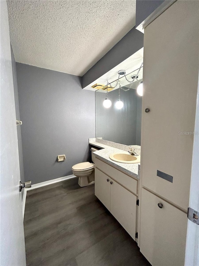 bathroom with toilet, vanity, a textured ceiling, wood finished floors, and baseboards