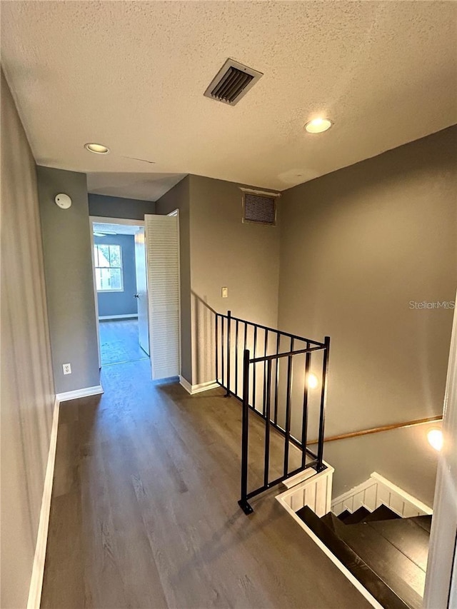 hallway featuring baseboards, visible vents, dark wood finished floors, a textured ceiling, and an upstairs landing