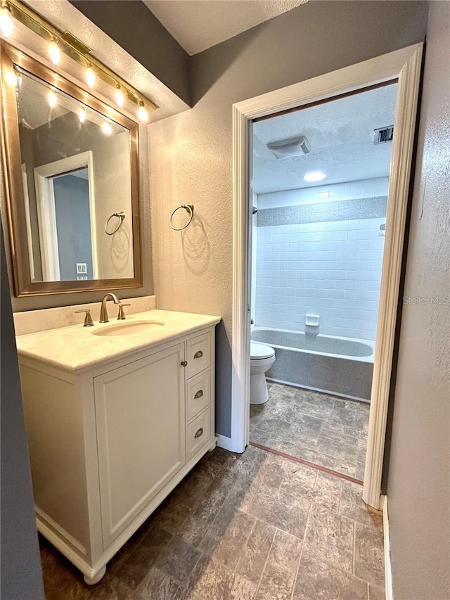 full bathroom with visible vents, a textured wall, toilet, stone finish flooring, and vanity