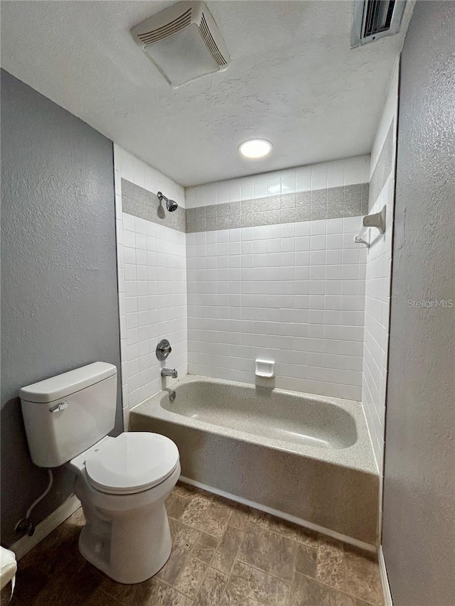 bathroom with a textured wall, visible vents, shower / tub combination, and toilet