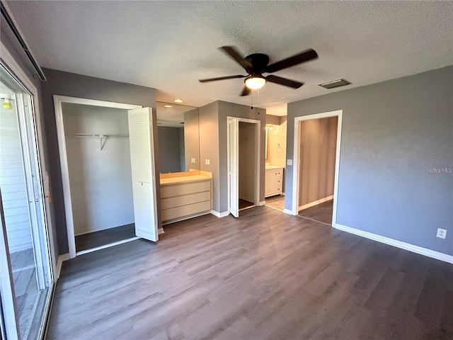 unfurnished bedroom featuring a textured ceiling, ceiling fan, dark wood-style flooring, visible vents, and baseboards