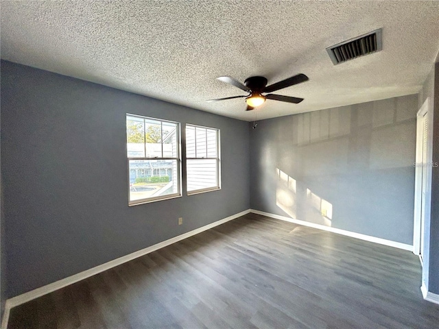 empty room with a textured ceiling, dark wood-type flooring, a ceiling fan, visible vents, and baseboards