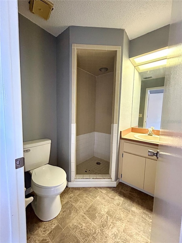 bathroom with toilet, a stall shower, a textured ceiling, and vanity