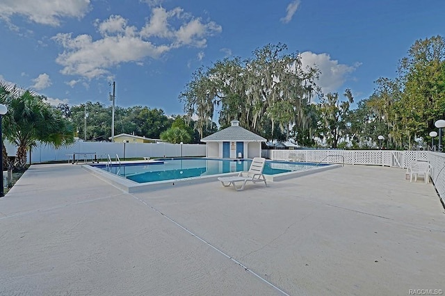 pool with a patio area, fence, and an outdoor structure