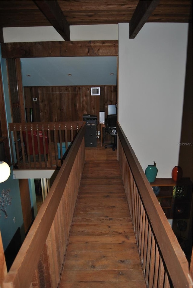 hallway featuring wood walls, visible vents, hardwood / wood-style floors, and beamed ceiling