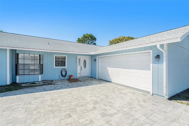 ranch-style house featuring a shingled roof, decorative driveway, and an attached garage