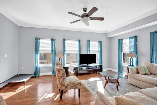 living area featuring light wood finished floors, baseboards, ornamental molding, and a ceiling fan