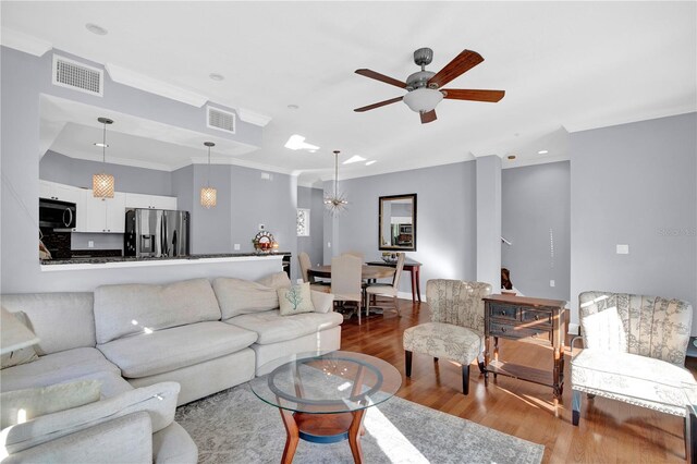 living room with ceiling fan, wood finished floors, visible vents, and crown molding