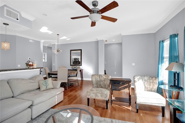 living room featuring baseboards, visible vents, a ceiling fan, ornamental molding, and wood finished floors