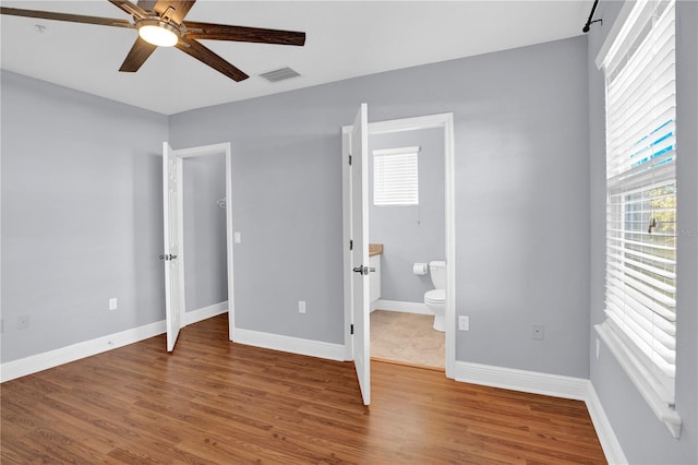 unfurnished bedroom with visible vents, ensuite bath, baseboards, and wood finished floors