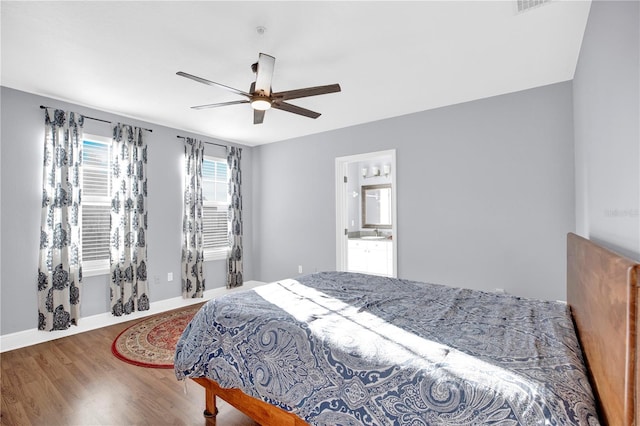 bedroom featuring a ceiling fan, ensuite bath, baseboards, and wood finished floors