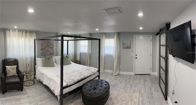 bedroom with light wood-type flooring, a barn door, visible vents, and recessed lighting