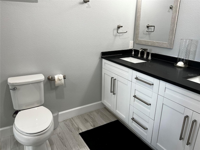 bathroom featuring double vanity, baseboards, toilet, wood tiled floor, and a sink