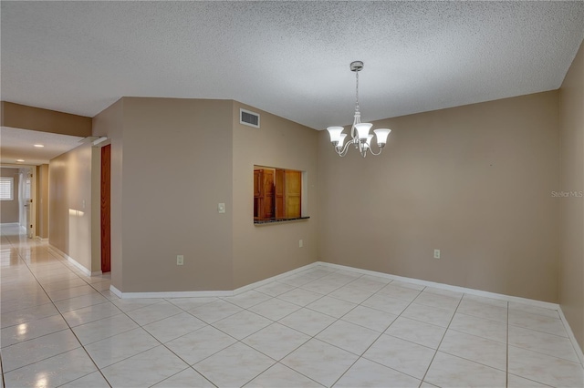 empty room with light tile patterned floors, a textured ceiling, visible vents, and a notable chandelier