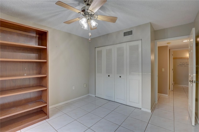 unfurnished bedroom with a textured ceiling, light tile patterned flooring, visible vents, baseboards, and a closet