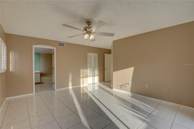 empty room with light tile patterned floors, a textured ceiling, visible vents, a ceiling fan, and baseboards