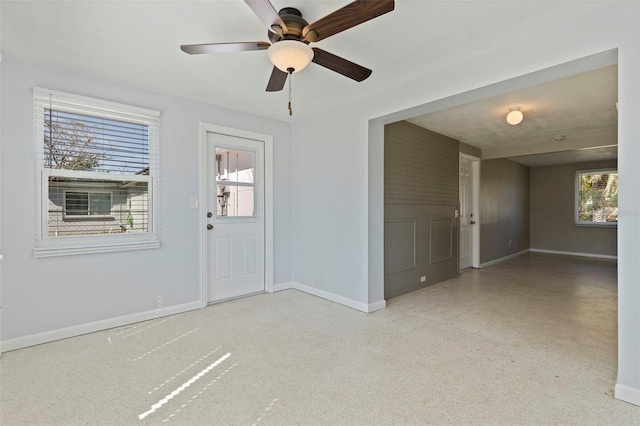 empty room with baseboards, a ceiling fan, and speckled floor