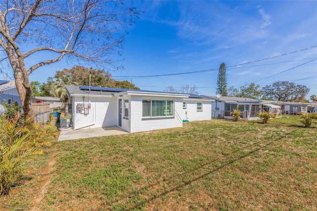 rear view of house with a patio, a lawn, a sunroom, roof mounted solar panels, and fence