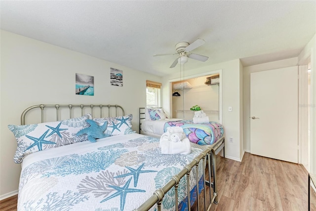 bedroom with a textured ceiling, wood finished floors, a ceiling fan, and a walk in closet