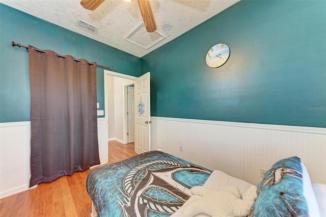 bedroom with a wainscoted wall, visible vents, and wood finished floors